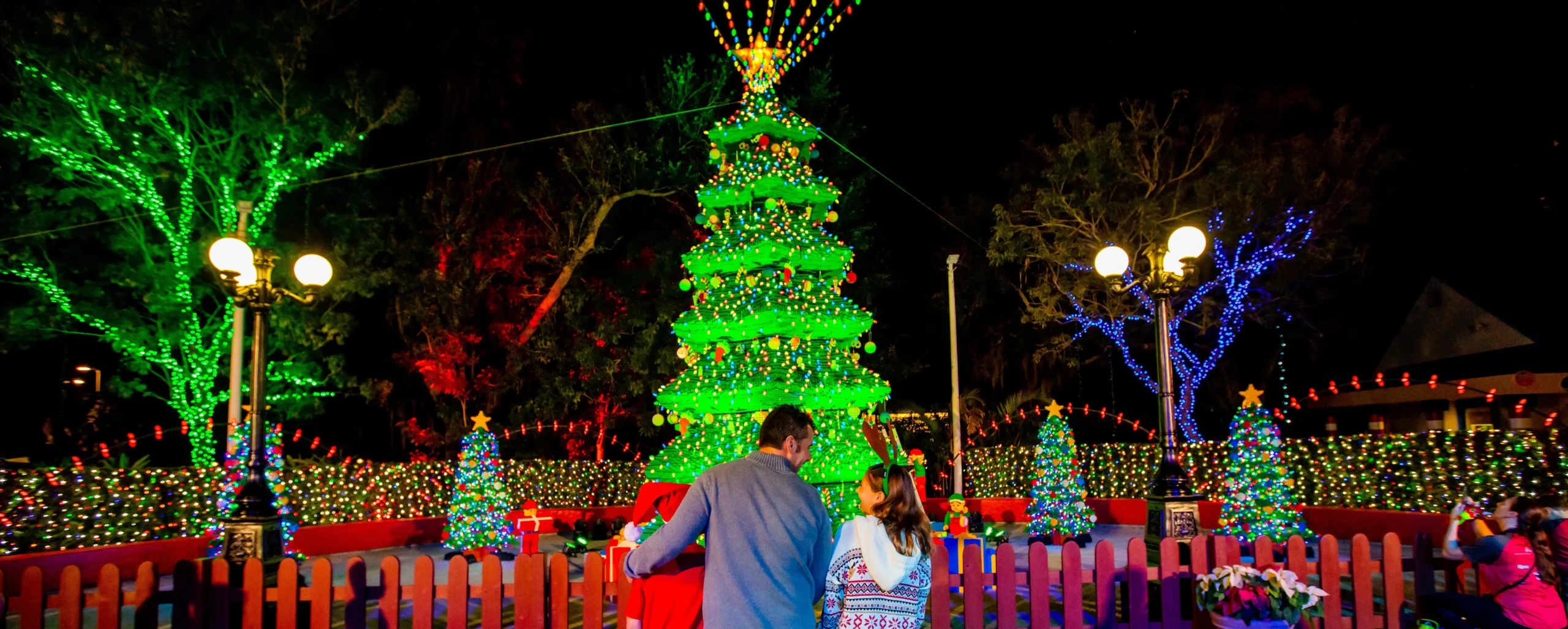 LEGOLAND Florida Christmas Bricktacular 2026: LEGO Santa Takes to the Sky 1 Family looking at the illuminated LEGO Christmas tree during the holidays at LEGOLAND Florida