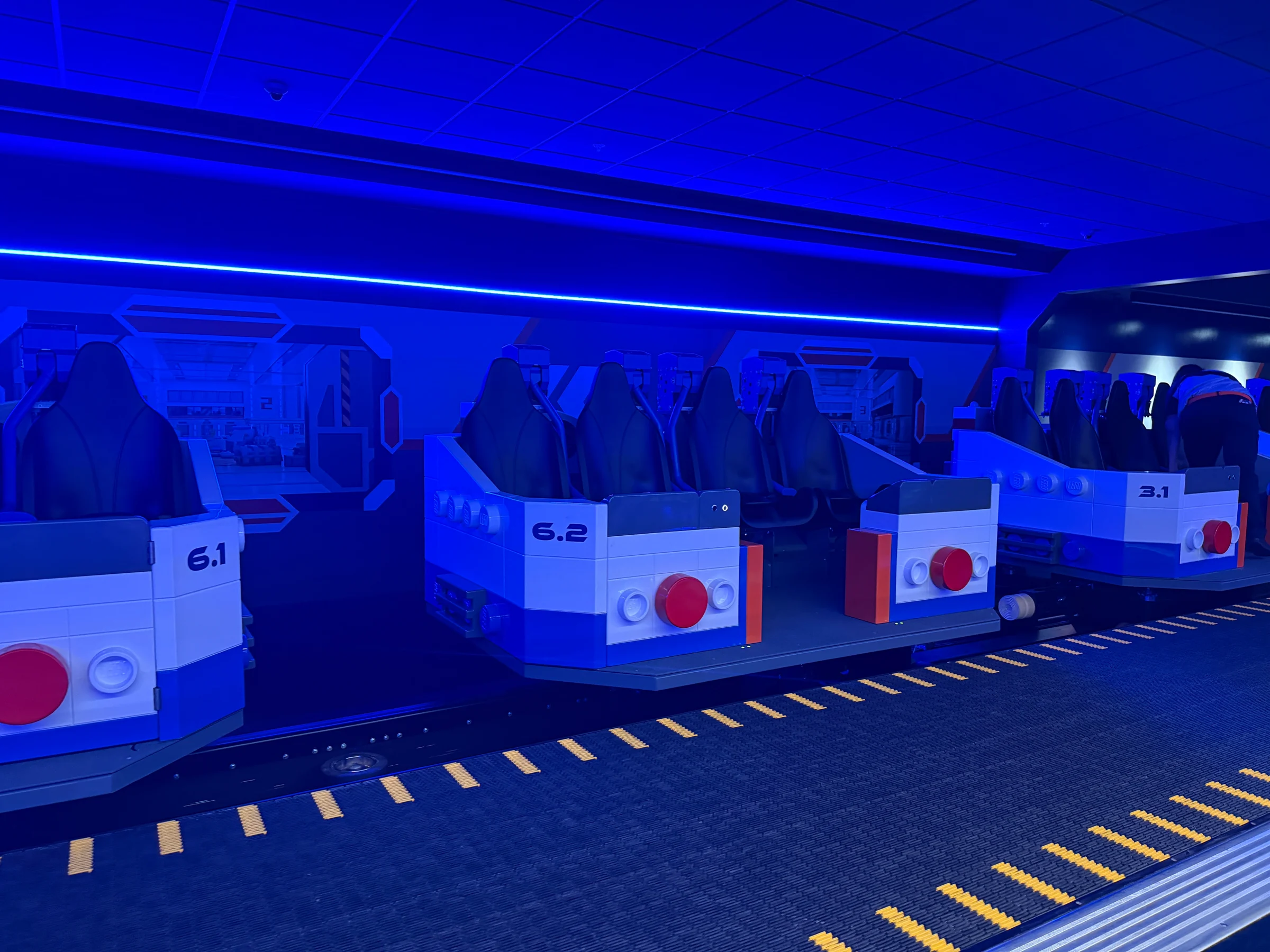 Inside Galacticoaster at LEGOLAND Florida: What Families Can Expect 3 Galacticoaster ride vehicles in a blue lit loading area at LEGOLAND Florida