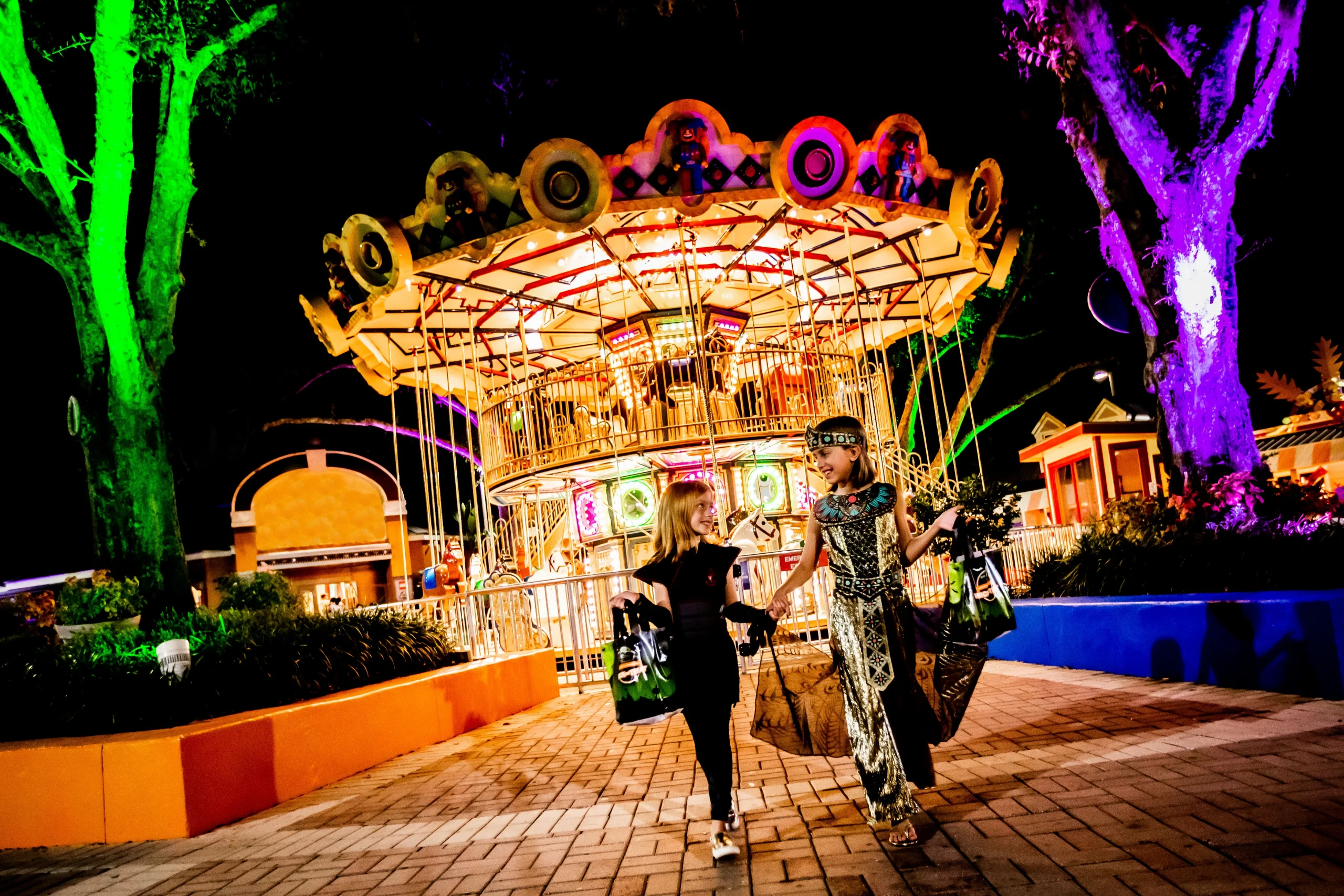 New for 2026: Brick or Treat Street at LEGOLAND Florida 5 Two children in Halloween costumes carrying treat bags near the illuminated carousel